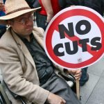 disabled-man-holding-no-cuts-sign (1)
